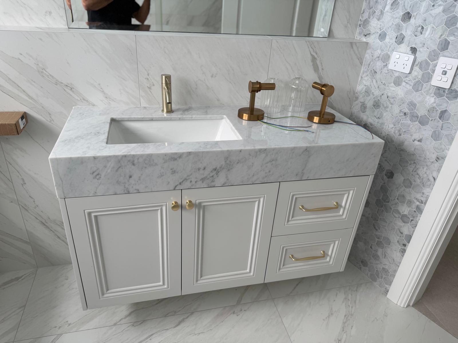 Wall-hung white vanity with a thick marble top, brass tapware and a hexagon mosaic feature wall.