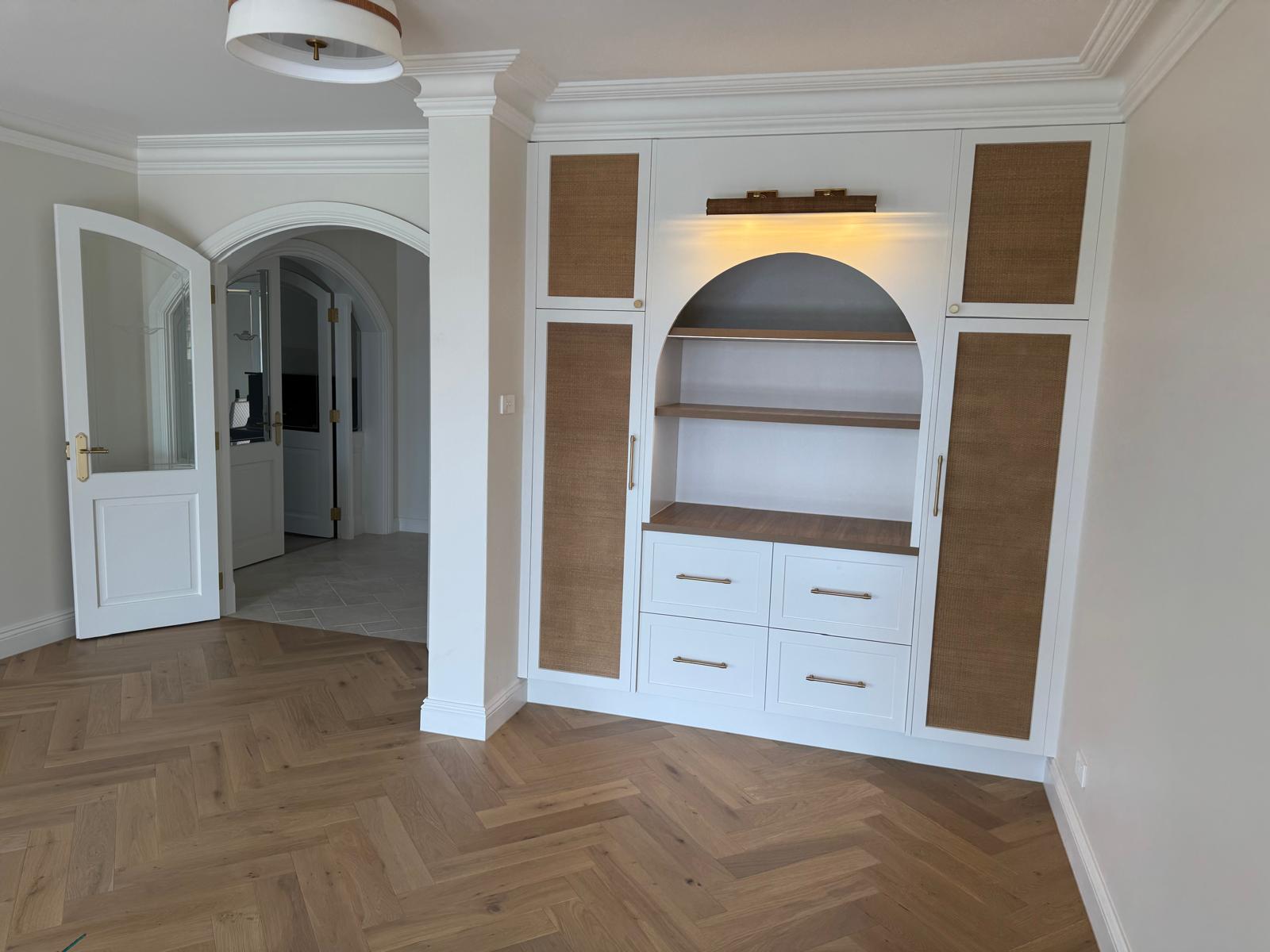 Custom white cabinetry with an arched open niche, timber shelves and rattan door panels.