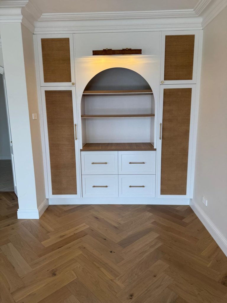 Built-in display unit with an arched shelf niche, drawers and rattan-panelled doors on herringbone flooring.