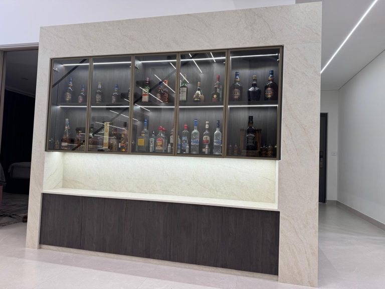 Stone-clad home bar with a lit glass-fronted display cabinet and dark timber base cabinets.