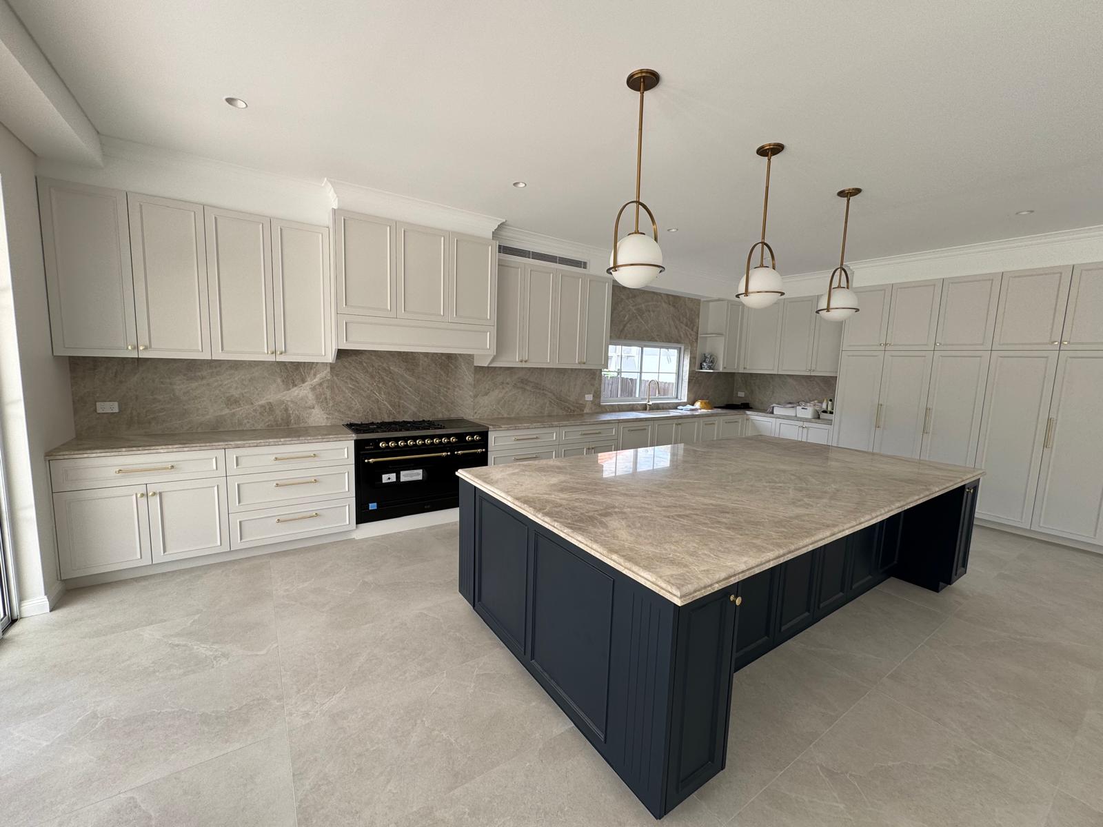 Kitchen with a large navy shaker island, stone benchtop and brass globe pendant lights.