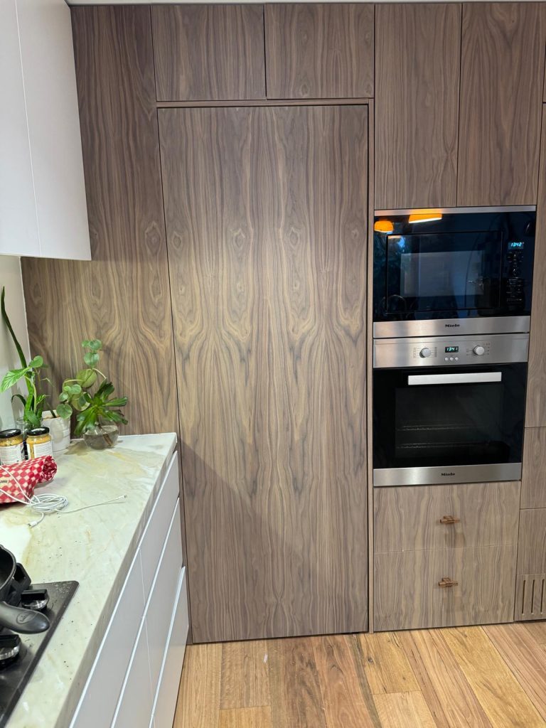 Walnut-veneer tall cabinets with built-in wall ovens beside a white kitchen run.