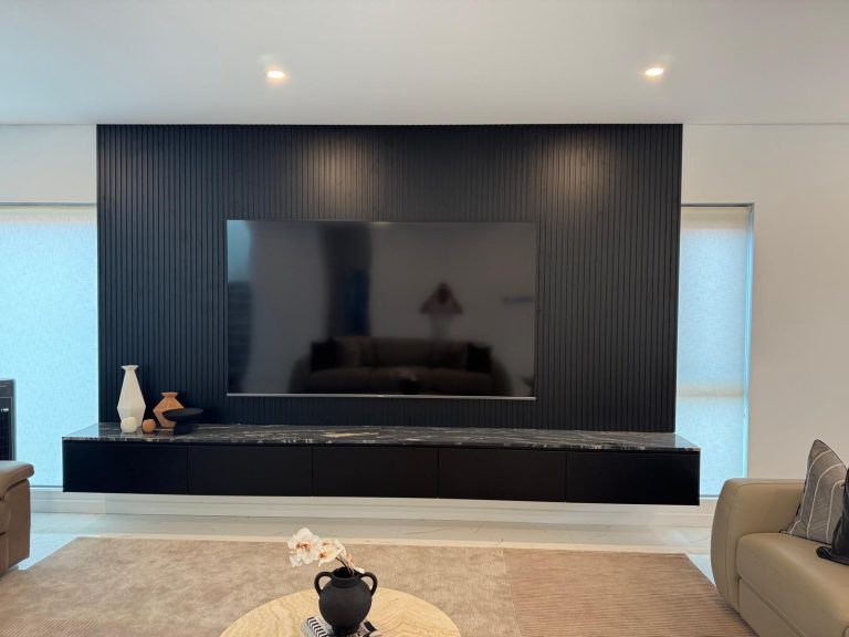 Black slatted TV feature wall with a long floating cabinet and stone top.