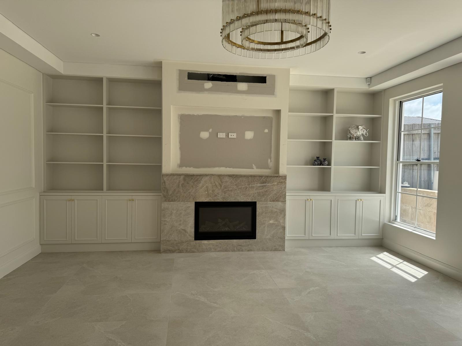 Living room with built-in white shelving and cabinets either side of a stone-clad fireplace.