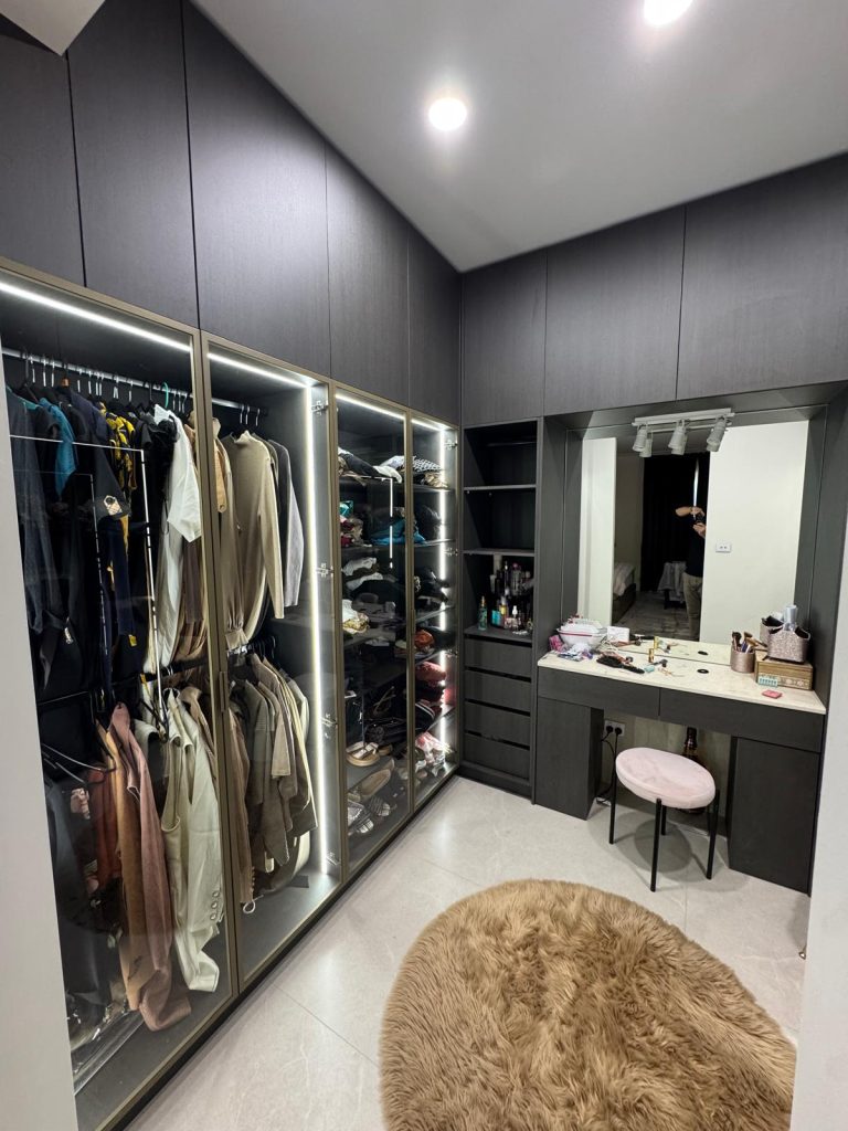 Walk-in wardrobe with lit glass-door cabinets and a built-in dressing table.